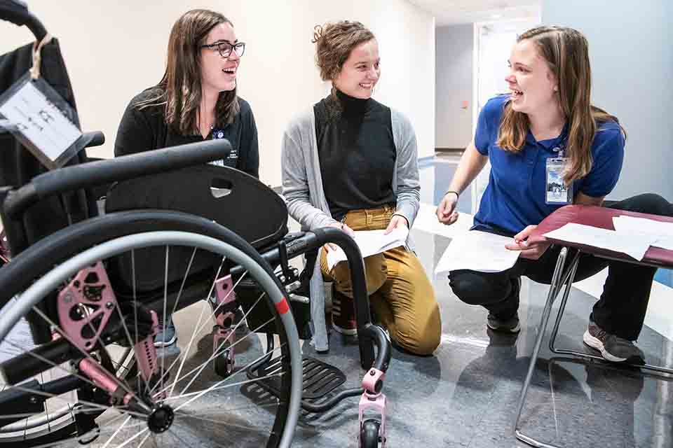 Students in PT class gathered around a wheelchair