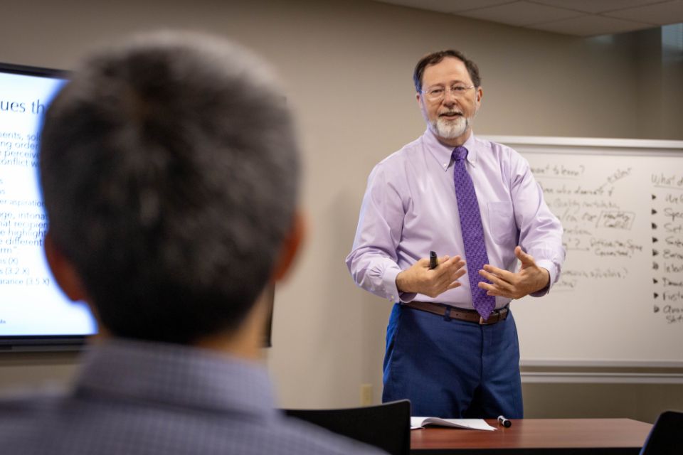 A man standing in the front of a room presenting to a participant