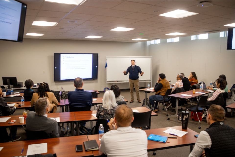a man standing and presenting in front of a group of people seated at desks