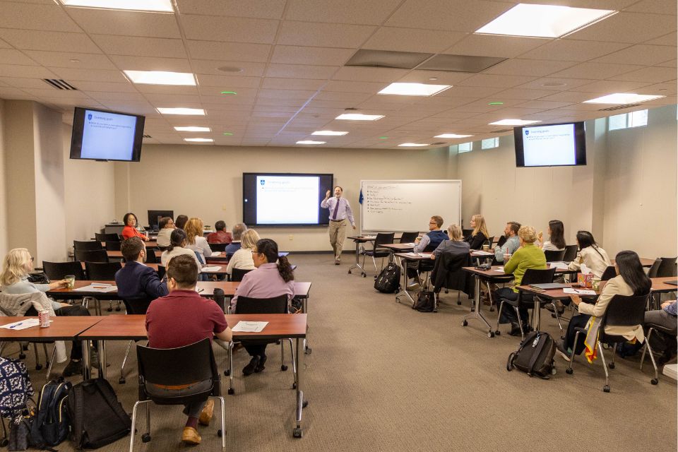 a man presenting in front of a group of people sitting at desks