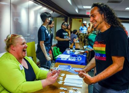 A student wearing an L G B T pride shirt talks to a volunteer running a table at an event.