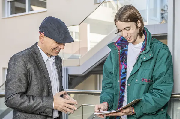 A professor and a student laugh and chat while looking at a student's notebook.