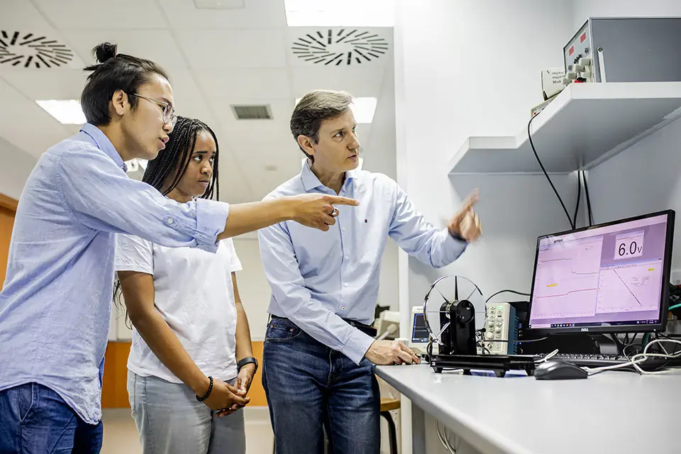 Two students and an instructor examine a computer screen while having a discussion.