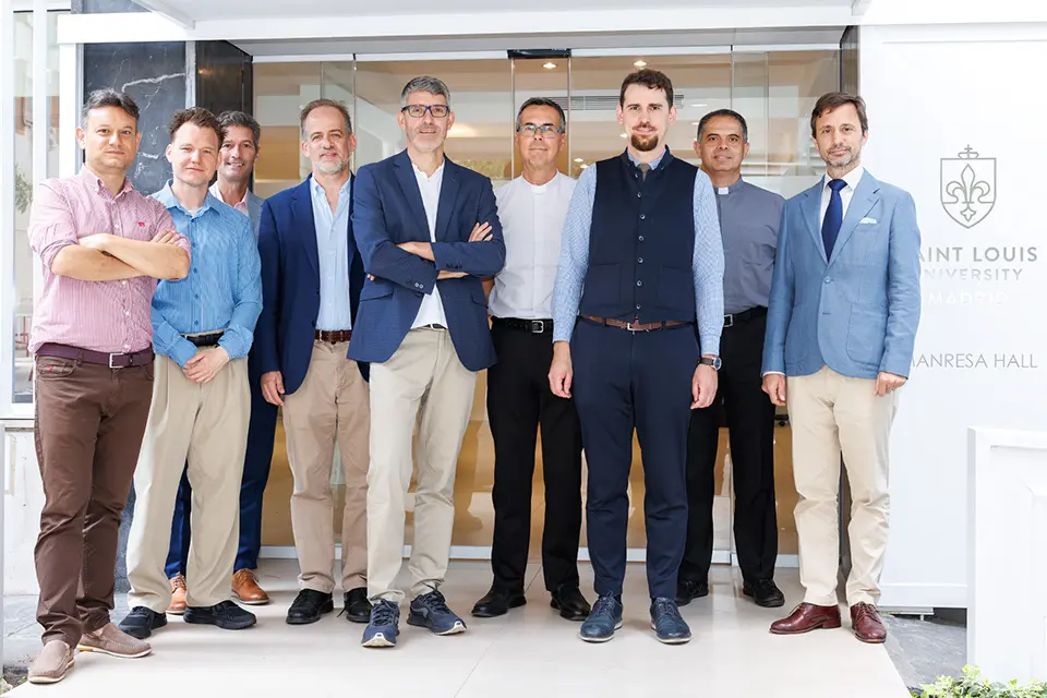 Nine individuals look at camera for group photo with building entrance in background.