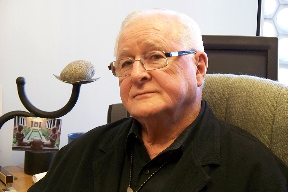 Dr. Raymond P. Benoit is sitting in a chair. He poses for a photo. He is wearing glasses and a black long-sleeve shirt.