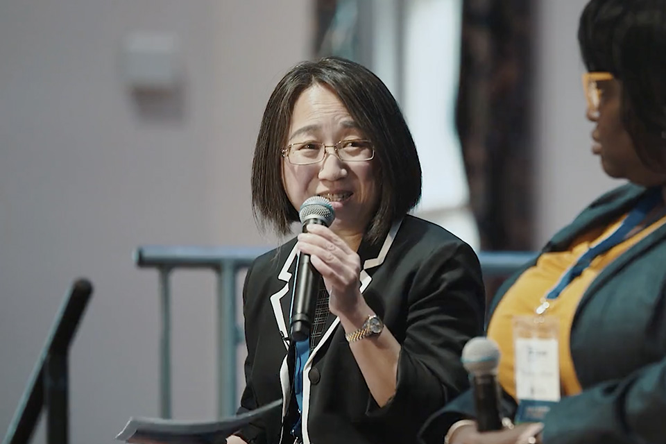 A woman sits and smiles while holding a microphone.